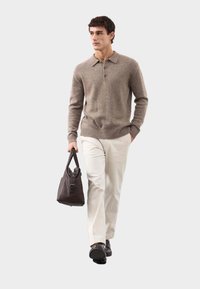 Brązowy sweter dzianinowy z kołnierzykiem, kremowe spodnie i ciemna torba. Gładka tekstura, dopasowany krój oraz solidne okucia na torbie.