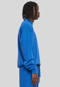 Felpa blu dal taglio morbido, con scollatura rotonda e polsini a costine. Il materiale sembra morbido. Indossata con pantaloni blu abbinati.