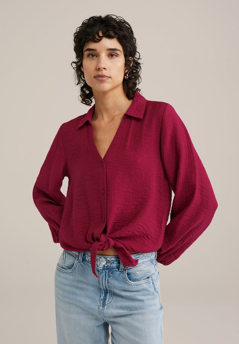 Bordeaux košulja s dugim rukavima i teksturiranom tkaninom, ovratnikom i čvorastim rubom, u kombinaciji s svijetloplavim hlačama visokog struka na neutralnoj pozadini.