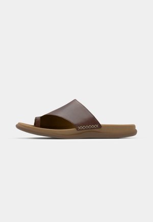 Sandal in pelle marrone a fascia con punta aperta, soletta morbida e arrotondata, e dettagli di cucitura testurizzati lungo la parte superiore. Suola in gomma leggera.