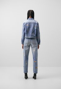 Completo giacca e pantaloni in denim, azzurro chiaro con design di patchwork astratti in vari colori. Vestibilità casual con giacca corta e pantaloni a vita alta.