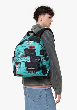 Mochila de tela en verde azulado con patrones gráficos en negro, que cuenta con un bolsillo delantero con cremallera y correas ajustables. Etiquetas de logo visibles en la parte delantera.