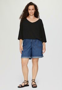 Schwarzes, weit geschnittenes V-Ausschnitt-Shirt mit Dreiviertelärmeln, kombiniert mit hochtaillierten, knielangen Jeansshorts mit Taschen und umgeschlagenen Säumen.