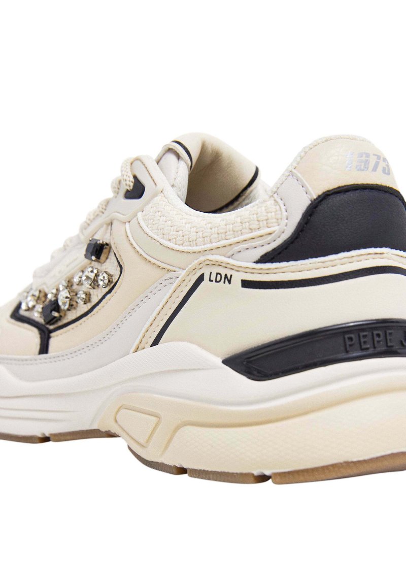 Sneaker beige e nera con pannelli testurizzati, strass decorativi sul lato e suola imbottita. Presenta il marchio "LDN" e "1973".