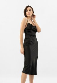 Vestito in satin nero con spalline sottili, scollatura a manicotto e silhouette aderente. Design di lunghezza media, texture liscia, senza pattern visibili o accessori metallici.