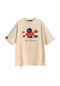 Camiseta de color beige claro de corte oversize con un estampado gráfico de tres figuras caricaturescas en negro, rojo y blanco, con mangas cortas y un ajuste relajado.