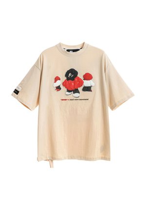 Camiseta de color beige claro de corte oversize con un estampado gráfico de tres figuras caricaturescas en negro, rojo y blanco, con mangas cortas y un ajuste relajado.