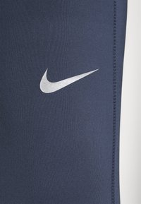 Gros plan d'un tissu bleu marine avec un logo swoosh blanc de Nike et des coutures visibles le long du bord.