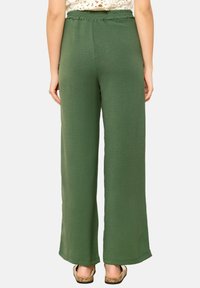 Olive green wide-leg pants with a textured fabric, elastic waistband, and straight silhouette, styled with flat, textured sandals.