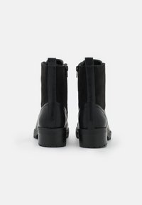 Botas negras hasta el tobillo con una combinación de cuero liso y ante. Presentan una punta redondeada, tacón grueso y un cierre de cremallera lateral. Se aprecian acentos texturizados.