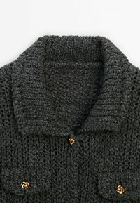 Cardigan en maille gris foncé avec col châle et boutons décoratifs dorés en forme de nœud sur les poches avant et la fermeture.