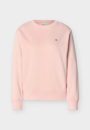 Svijetloružičasta trenirka s okruglim izrezom, dugim rukavima, rebrastim manžetama i rubom te malim vezenim logotipom na lijevoj strani prsa.