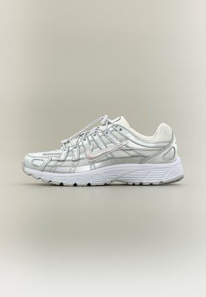 Chaussure de course Nike blanche et gris clair avec panneaux en mesh, logo swoosh latéral, et semelle blanche texturée sur un fond neutre.