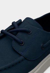 Παπούτσι από σουέτ σε ναυτικό μπλε με κορδόνια και στρογγυλά οπές, αντίθετη ραφή, λεία υφή και λευκή λαστιχένια σόλα.