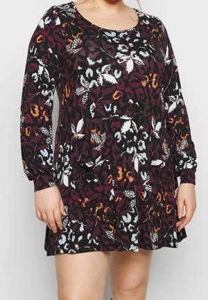 Personne grande taille portant une robe à manches longues, longueur genou, avec un motif floral sombre et imprimé animal abstrait.