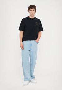 Black short-sleeve t-shirt with chest logo, paired with light blue loose-fit jeans and white sneakers. Plain background highlights outfit.