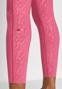 Ροζ αθλητικά κολάν με υφή σχεδίασης. Διαθέτουν ορατό λογότυπο Nike Swoosh, ραφές σε αντίθεση και εφαρμοστή γραμμή.