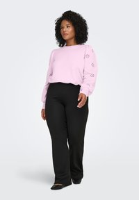 Light pink sweatshirt with cut-out detailing on sleeves, paired with black pants. The fabric appears soft with a relaxed fit and ribbed cuffs.