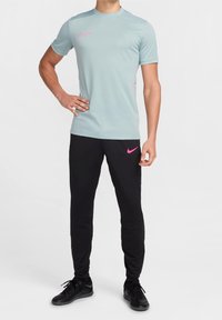 Vaaleansininen lyhythihainen Nike-paita, jossa on vaaleanpunaisia yksityiskohtia, yhdistetty mustiin Nike-housuihin, joissa on vaaleanpunainen logo, ja mustiin urheilukenkiin.