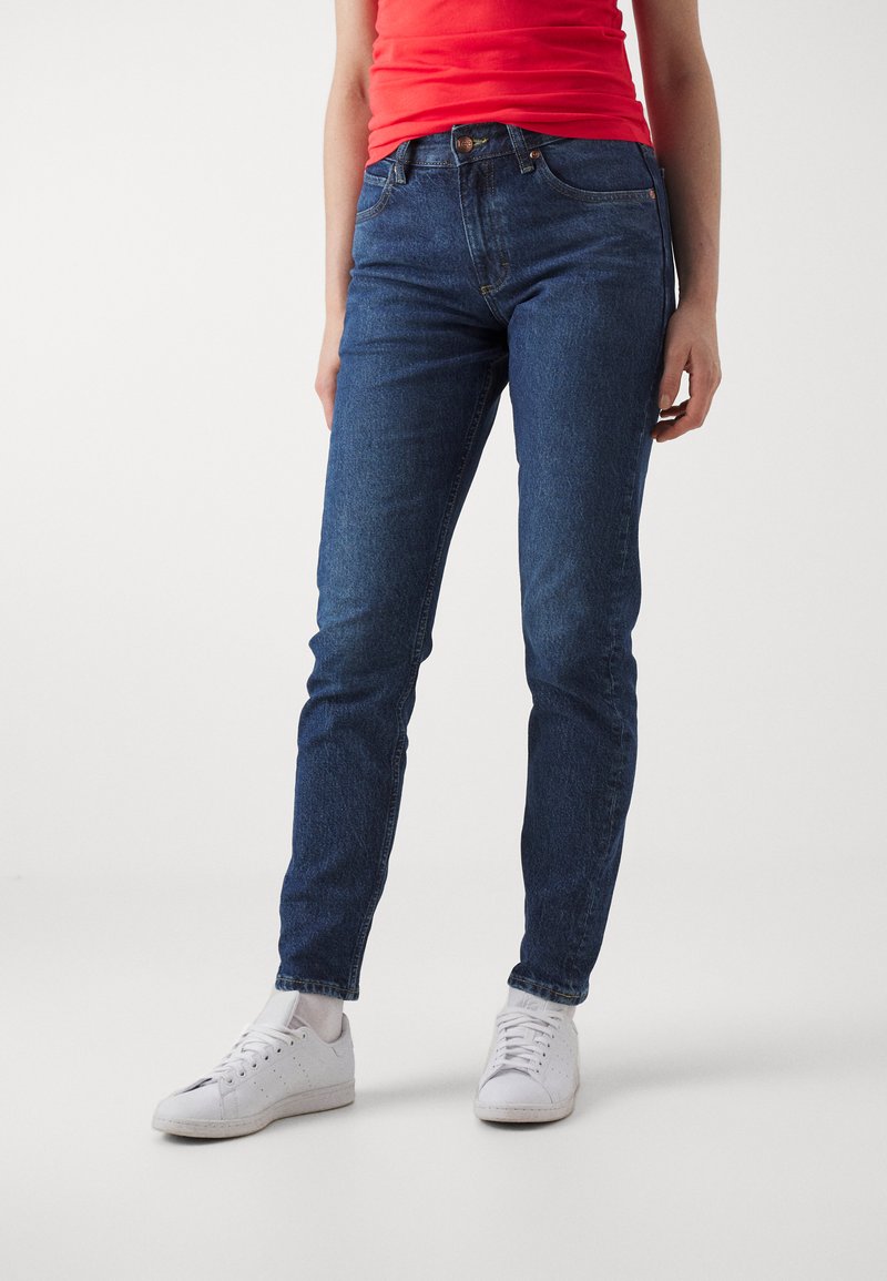 Slim-fit modré jeans v denimovej tkanine, s dizajnom piatich vreciek, pútkami na opasok a zipsom. V kombinácii s bielymi teniskami.