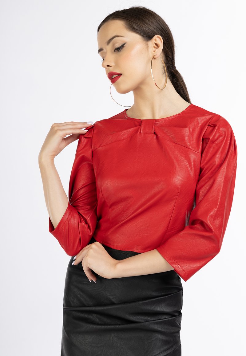 Blusa de cuero roja con mangas tres cuartos, escote redondo y sutiles pliegues en los hombros. Combinada con una falda de cuero negra.