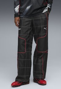 Pantaloni sport negri cu accente roșii și cusături albe, având un model în rețea și un logo pe coapsă. Asortați cu adidași roșii.