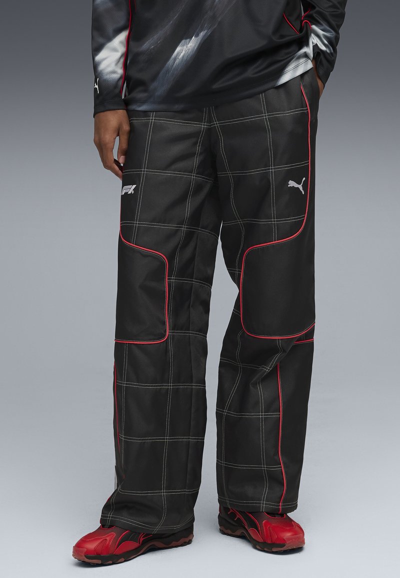 Pantaloni sport negri cu accente roșii și cusături albe, având un model în rețea și un logo pe coapsă. Asortați cu adidași roșii.