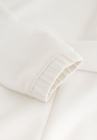 Gros plan sur une manche en tissu blanc avec un poignet élastique et des coutures visibles sur un vêtement doux.