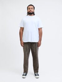 Vit bomull t-shirt, lös passform. Bruna texturerade byxor med ett subtilt mönster. Svartvita sneakers fulländar outfiten. Enkla bakgrund.