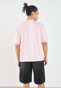 Kortermet, oversized rosa bomull t-skjorte med rund hals, parret med svarte denimshorts, som har baklommer og løs passform.