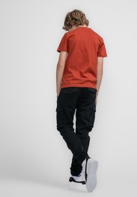 Rode katoenen T-shirt met ronde hals, gecombineerd met zwarte cargobroeken met zijzakken, afgewerkt met zwart-witte sneakers.