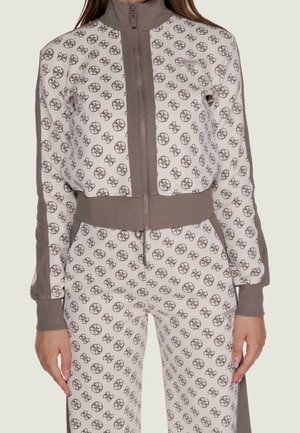 Ensemble veste zippée et pantalon blanc et taupe avec motif de logo circulaire répété et poignets et ceinture côtelés, porté par une personne.