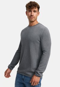 Grå langermet genser i teksturert strikk, med rund hals og tettsittende mansjetter, kombinert med blå jeans.