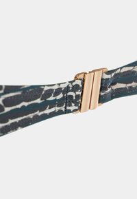 Modieus accessoire met een stoffen band met een blauw-wit patroon en een roségouden metalen klip. De textuur is glad en rekbaar.