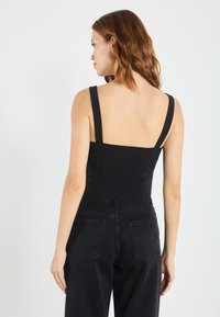 Svart bodysuit med brede stropper, tettsittende design, glatt tekstur og firkantet rygg, kombinert med høyhalsede svarte denimjeans.