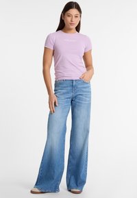 Lichtpaarse aansluitende T-shirt met 'GUESS JEANS' logo, gecombineerd met losse, lichtgewassen denim jeans met een hoge taille en wijde pijpen.