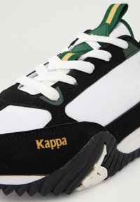 Zapatilla en blanco y negro con acentos en verde y amarillo. Presenta una parte superior de ante, cordones blancos y una suela de goma. Detalle del logo dorado "Kappa".