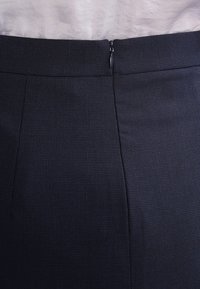 Marinblå blyertskjol med strukturerad tyg, sidoknäppning och figursydd silhuett. Har ett subtilt randigt mönster över hela.