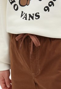 Kremowa bluza z grafiką, połączona z brązowymi spodniami ze sznurkiem w pasie i widocznymi detalami stębnowania.