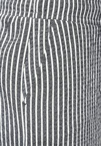 Tissu noir et blanc à rayures verticales avec un tissage texturé. Présente des rayures étroites et larges, créant un motif contrasté.