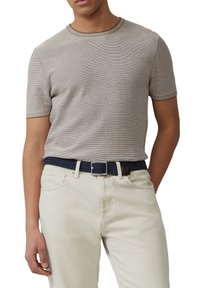 Man met een beige T-shirt met korte mouwen en fijne strepen, in zijn off-white broek gestopt, met een marineblauwe gevlochten riem met een zilveren gesp.