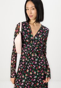 Robe à imprimé floral avec des manches longues, présentant un détail de nœud à la taille, fabriquée en tissu léger avec un fond noir et des motifs colorés.