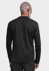 Langärmliges schwarzes Shirt mit glatter Textur, rundem Halsausschnitt und geradem Saum. Die Rückseite zeigt ein sauberes, minimalistisches Design ohne Logos.
