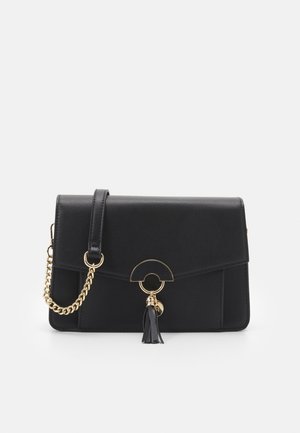 Czarna torebka z sztucznej skóry z złotym łańcuszkiem, klapką, okrągłym elementem dekoracyjnym oraz frędzlami na przodzie.
