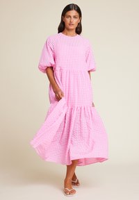Rosa, lagdelt midikjole laget av teksturert stoff med rutedesign. Rund hals og korte puffermarmer, stylet med hvite sandaler.