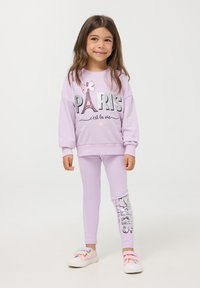 Liliowa bluza z napisem "PARYŻ" i wzorem wieży Eiffla; pasujące liliowe legginsy z błyszczącym napisem "PARYŻ" po boku; codzienne obuwie.