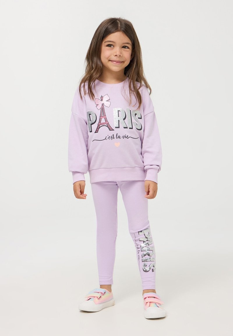 Liliowa bluza z napisem "PARYŻ" i wzorem wieży Eiffla; pasujące liliowe legginsy z błyszczącym napisem "PARYŻ" po boku; codzienne obuwie.