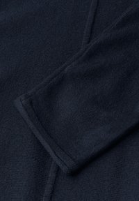 Marineblaue Stoff mit glatter Textur und sichtbaren Nähten. Besitzt einen umgeschlagenen Ärmel, der das weiche Material und die klaren Linien betont.