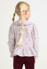 Blusa viola chiara con motivi floreali, colletto arricciato e polsini elastici, abbinata a pantaloni in velluto a coste bordeaux. Vista posterior.