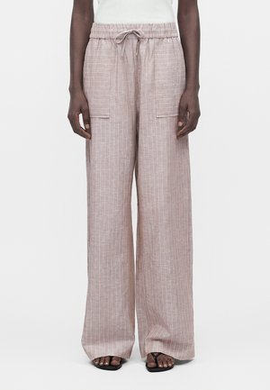 Szerokie beżowe lniane spodnie z białymi pionowymi paskami, elastycznym pasem, przednimi kieszeniami nakładanymi, noszone z czarnymi sandałami i białym topem.